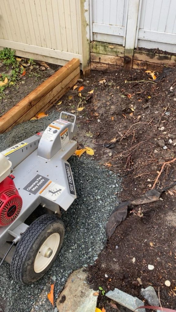 Portable concrete mixer on wheels in a backyard beside a wooden garden bed and fence.