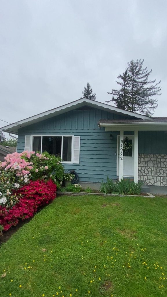 Blue ranch-style house with white trim, front door showing vertical address 34922, and a vibrant pink/red azalea garden in the yard.