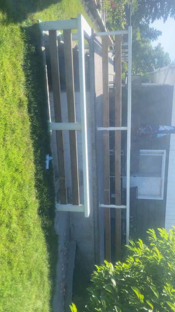 Unfinished wooden deck railing frame with white posts on a grassy backyard, beside a house with steps and a window.