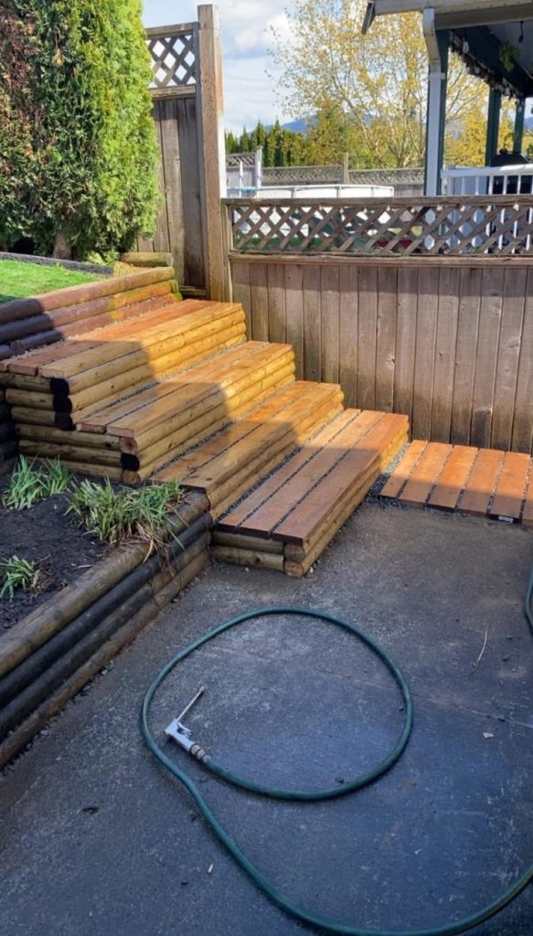 Wooden backyard stairs beside a lattice fence, with a coiled green garden hose on the pavement nearby.