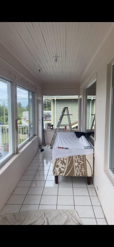 Sunroom or enclosed porch under renovation with a ladder, tools, and a covered sofa on white tile flooring.